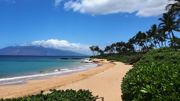 Une plage avec une eau d’un bleu limpide, un rivage sablonneux et une montagne en arrière-plan.