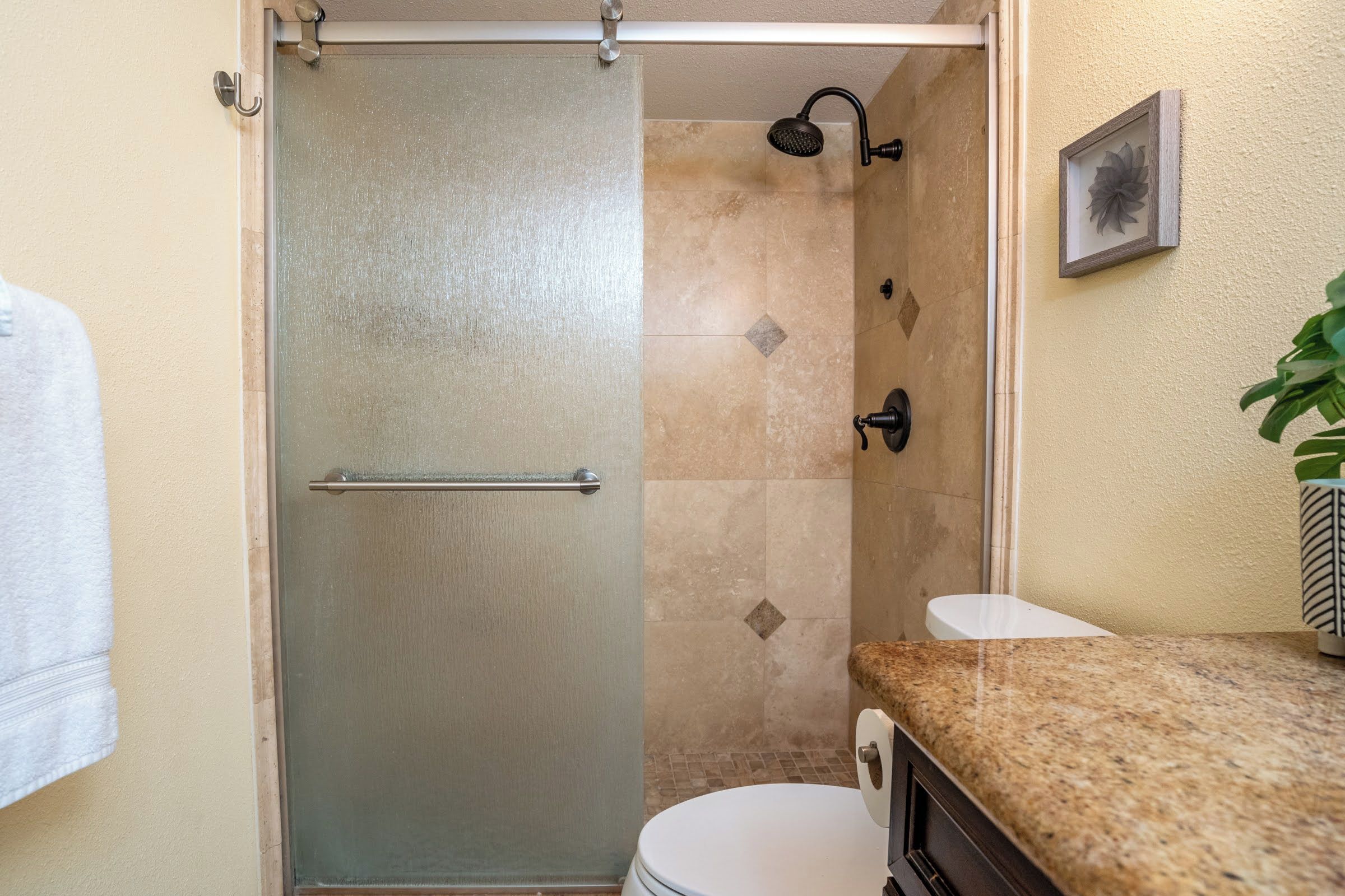 Ein Badezimmer mit Duschabtrennung aus Glas, Toilette und Waschbecken mit Granitplatte.