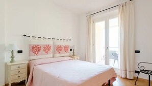 A bedroom with a bed, nightstands, a chair, and a view of the outdoors.