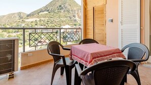 A balcony with a table and chairs, a view of a mountain, and a closed door.