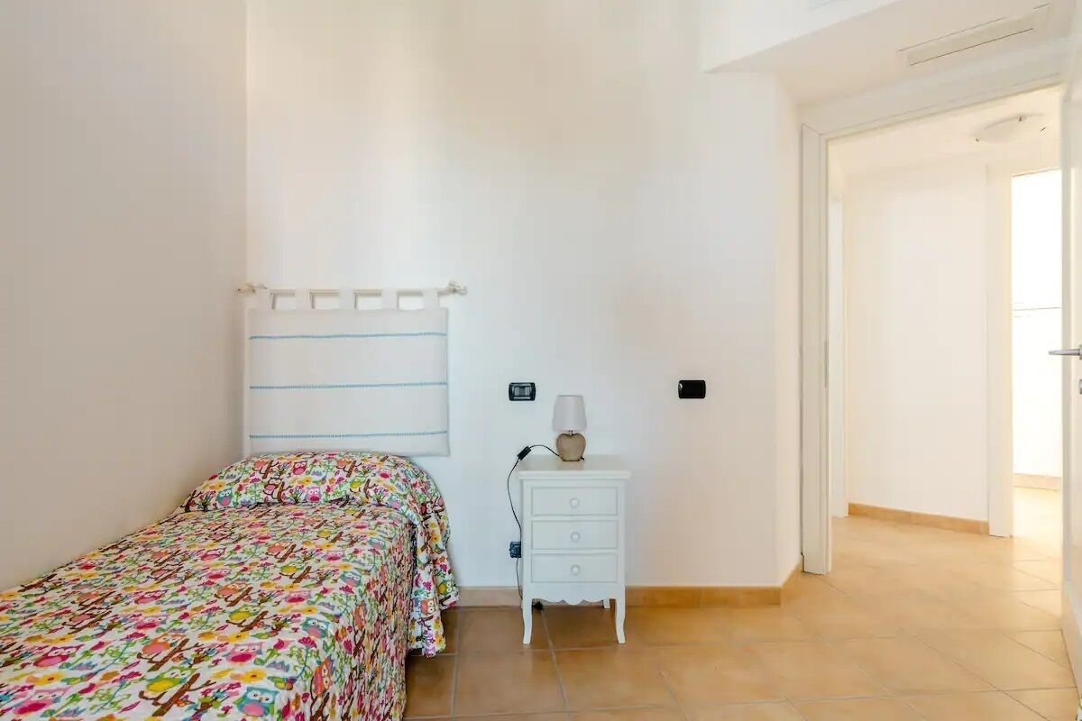 A bedroom with a bed, a nightstand, and a wall-mounted lamp.