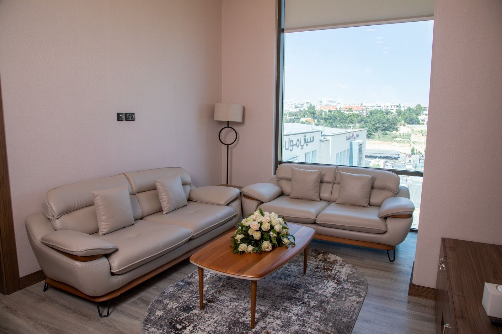 Una sala de estar moderna con dos sofás beige, una mesa de centro de madera y un amplio ventanal con vistas a la ciudad.