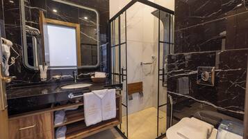 Une salle de bain moderne avec un meuble-lavabo en marbre noir, une douche à parois de verre et un meuble en bois où sont rangées les serviettes.