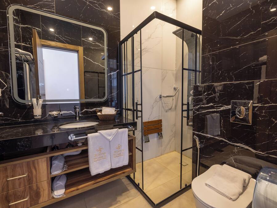 Une salle de bain moderne avec un meuble-lavabo en marbre noir, une douche à parois de verre et un meuble en bois où sont rangées les serviettes.