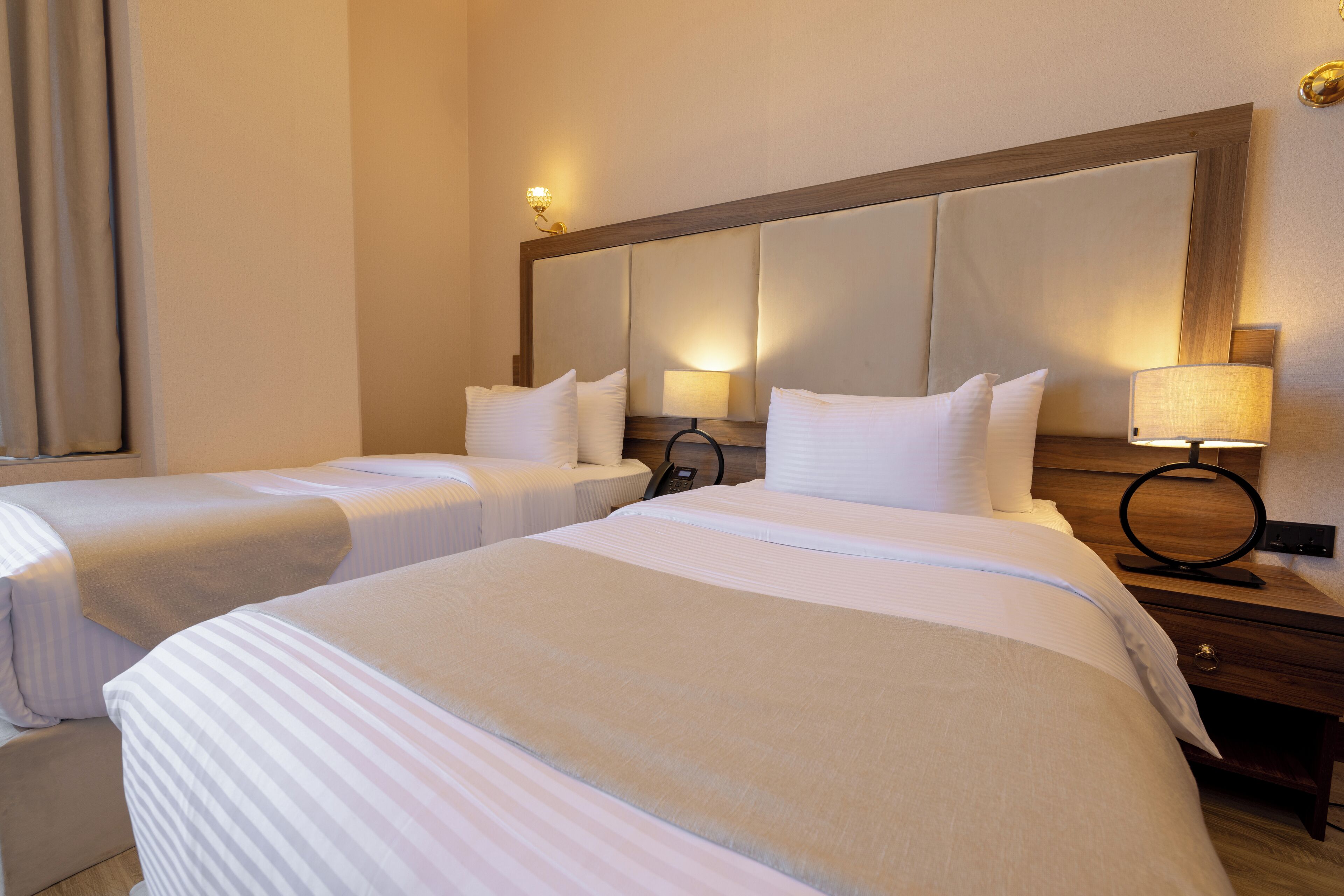 A hotel room with two single beds, each with a pillow and a bedside table with a lamp.