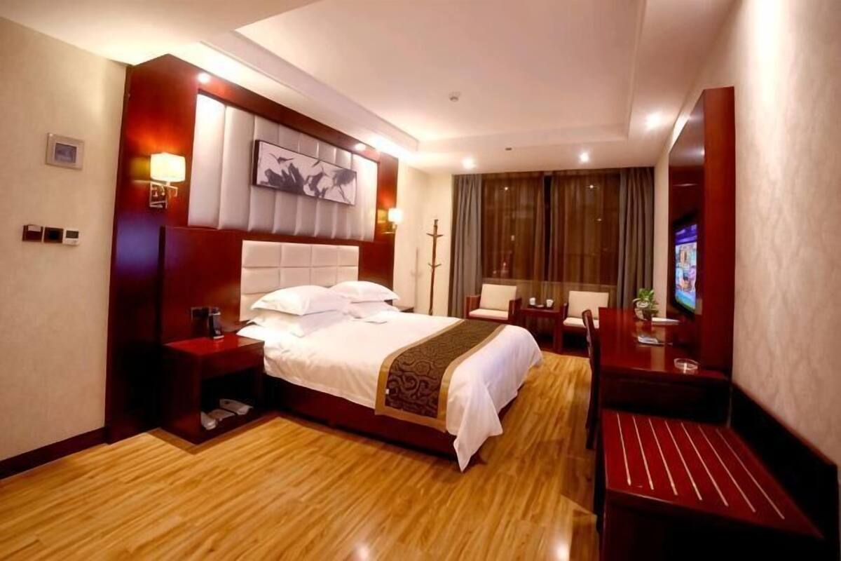 Quarto de hotel com cama, mesas de cabeceira, escrivaninha, cadeira, televisão e uma janela grande.