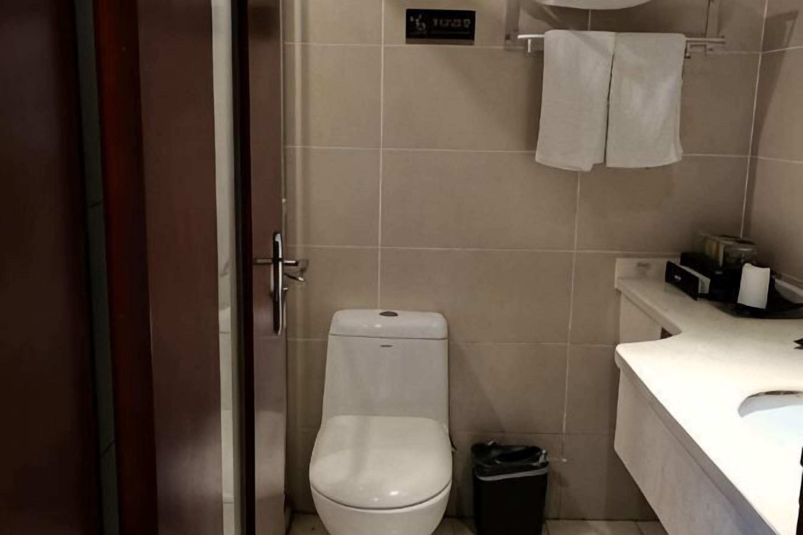 Un baño con inodoro, un cubo de basura, un lavamanos y un perchero para toallas.