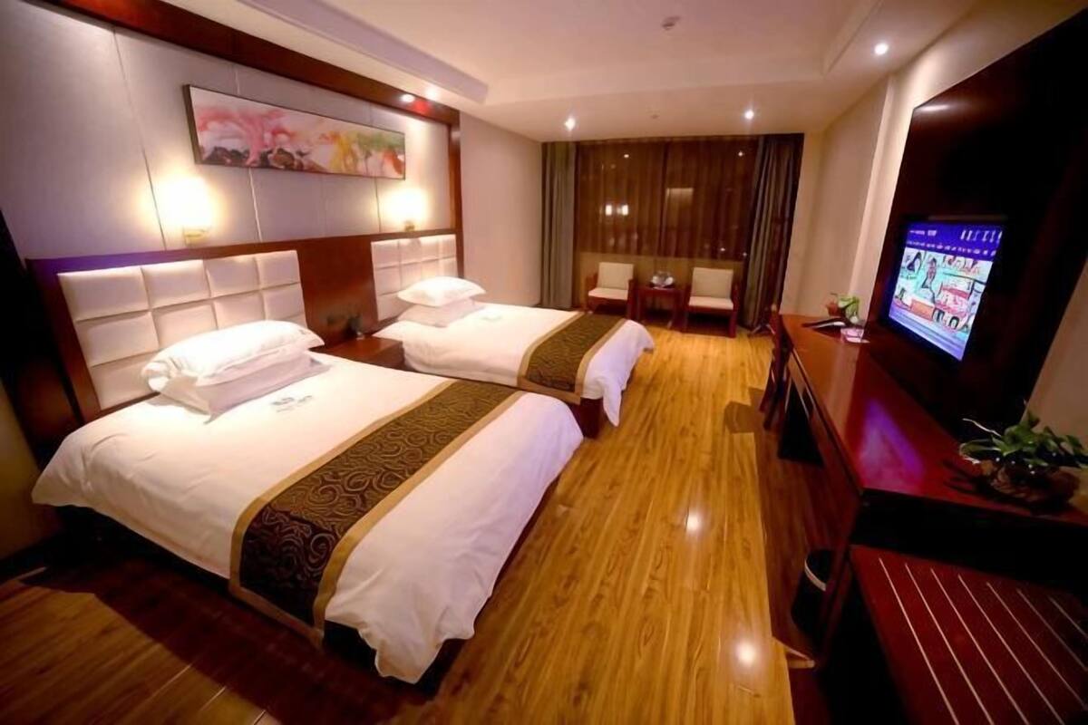 Quarto de hotel com duas camas, televisão, escrivaninha e uma janela grande.