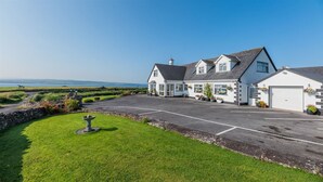 A large white building with a garage, surrounded by a well-maintained lawn and a stone wall. - Sea Haven - Stunning Sea Views! (County Clare)