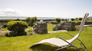 A grassy area with a lounge chair and stone structures with spherical tops, overlooking a body of water and distant landscape. - Sea Haven - Stunning Sea Views! (County Clare)