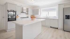 A modern kitchen with white cabinetry, a central island, a built-in oven, and a stainless steel refrigerator. - Sea Haven - Stunning Sea Views! (County Clare)