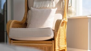 A wicker chair with a cushion and a white pillow, positioned near a white nightstand and a glass door. - Sea Haven - Stunning Sea Views! (County Clare)