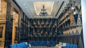 A modern lobby with blue sofas arranged in a semi-circle, a chandelier, and a geometric wall design. - Bel-La Monde Hotel Chhattarpur South Delhi (New Delhi)