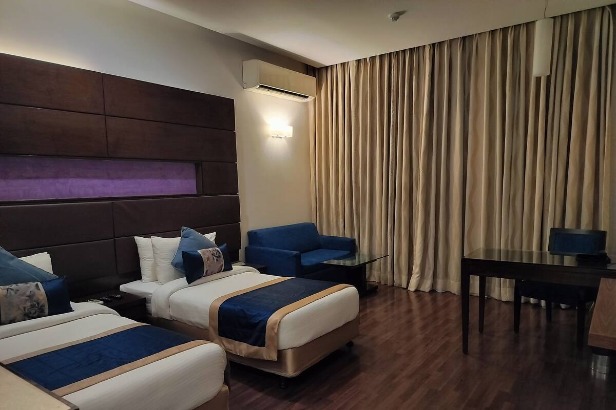 Habitación de hotel con dos camas, un sofá, una mesita y un televisor.