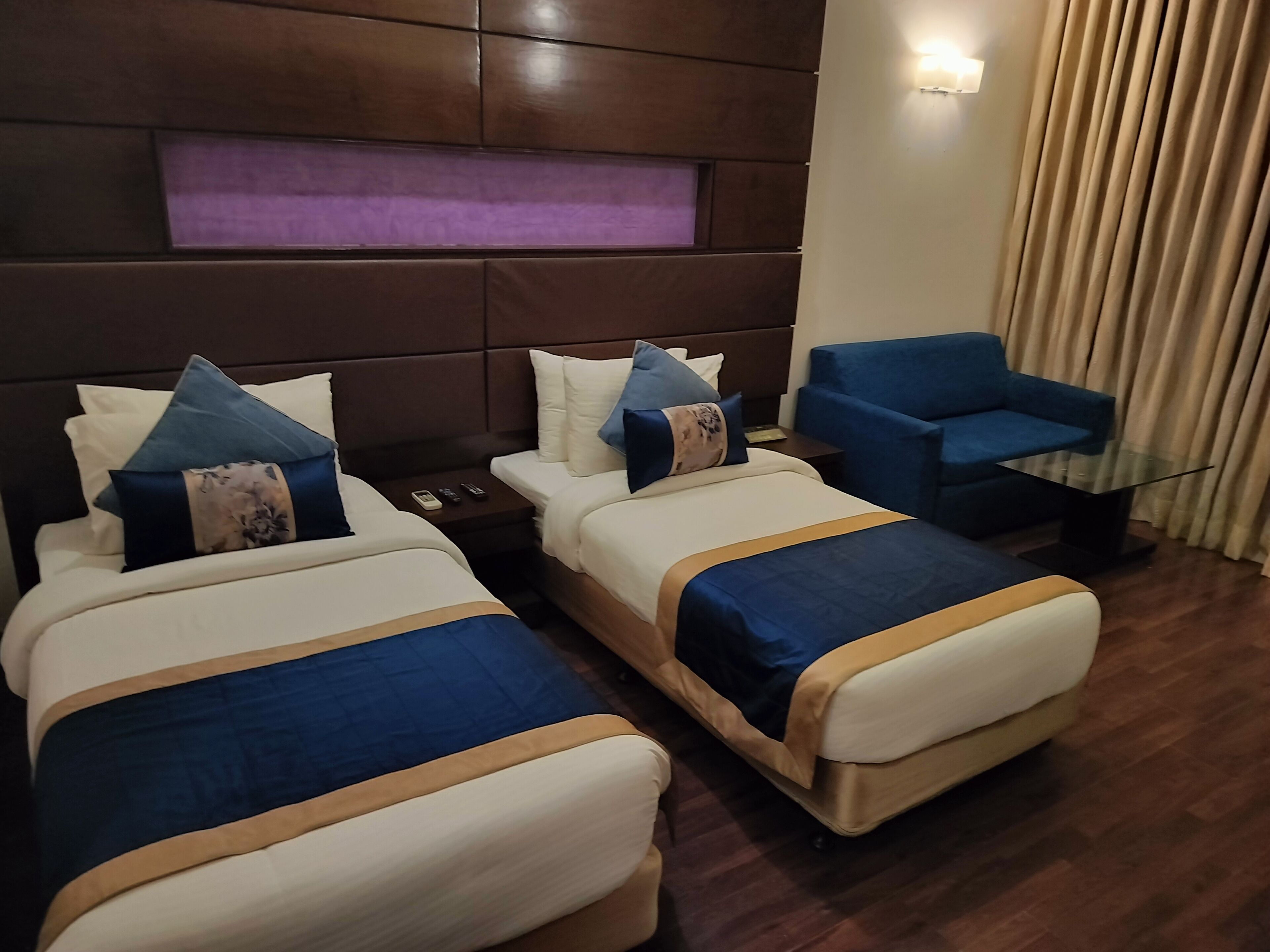 A hotel room with two beds, a blue armchair, and a glass coffee table.