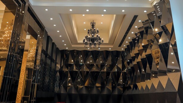 A spacious lobby with a grand chandelier, multiple seating areas, and a geometric wall design. - Bel-La Monde Hotel Chhattarpur South Delhi (New Delhi)
