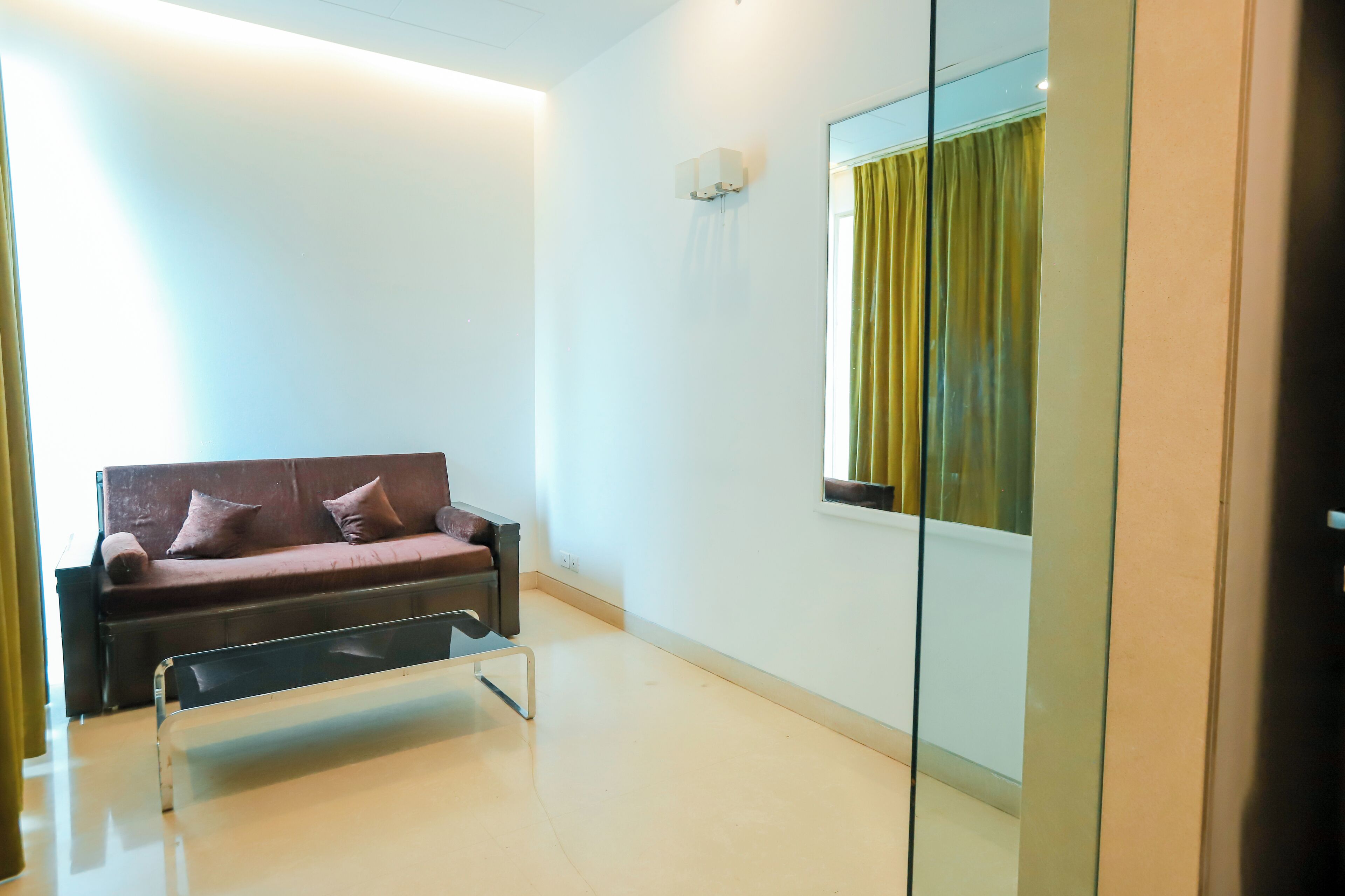 A modern room with a sofa, a small table, a mirror, and a window with curtains.