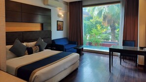 A modern hotel room with a large bed, a sofa, a dining table, and a view of the outdoors. - Bel-La Monde Hotel Chhattarpur South Delhi (New Delhi)