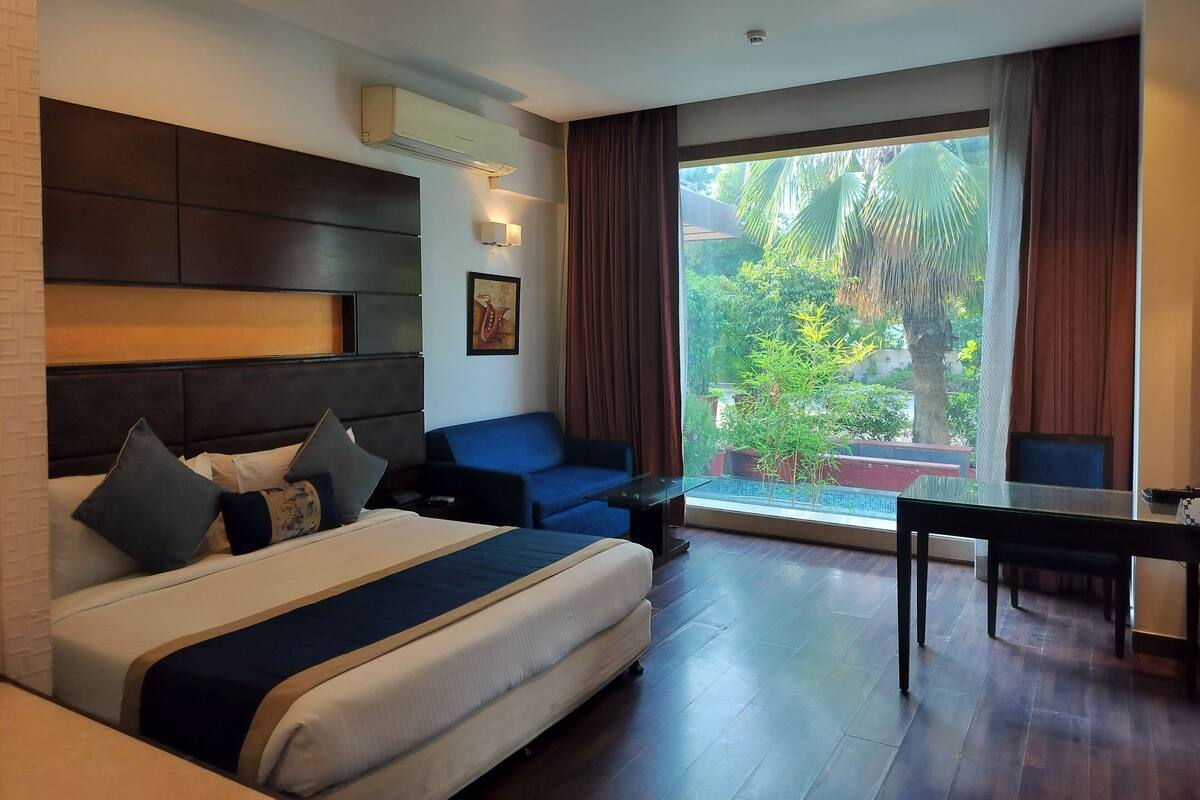 Habitación de hotel moderna con una cama grande, un sofá, una mesa de comedor y vistas al exterior.