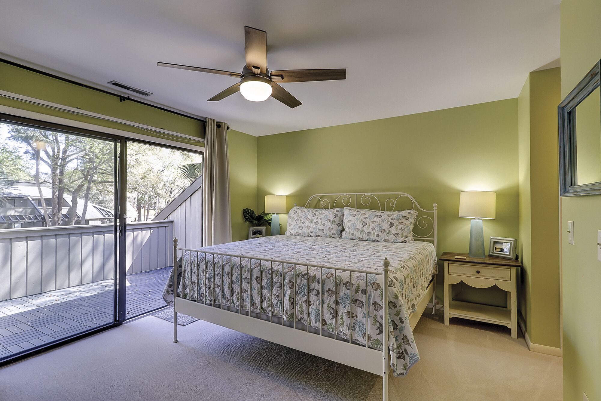 A bedroom with a bed, a nightstand, a ceiling fan, a window with a view, and a balcony.