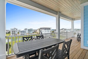 A covered outdoor deck with a table and chairs, overlooking a residential area with houses and a body of water.