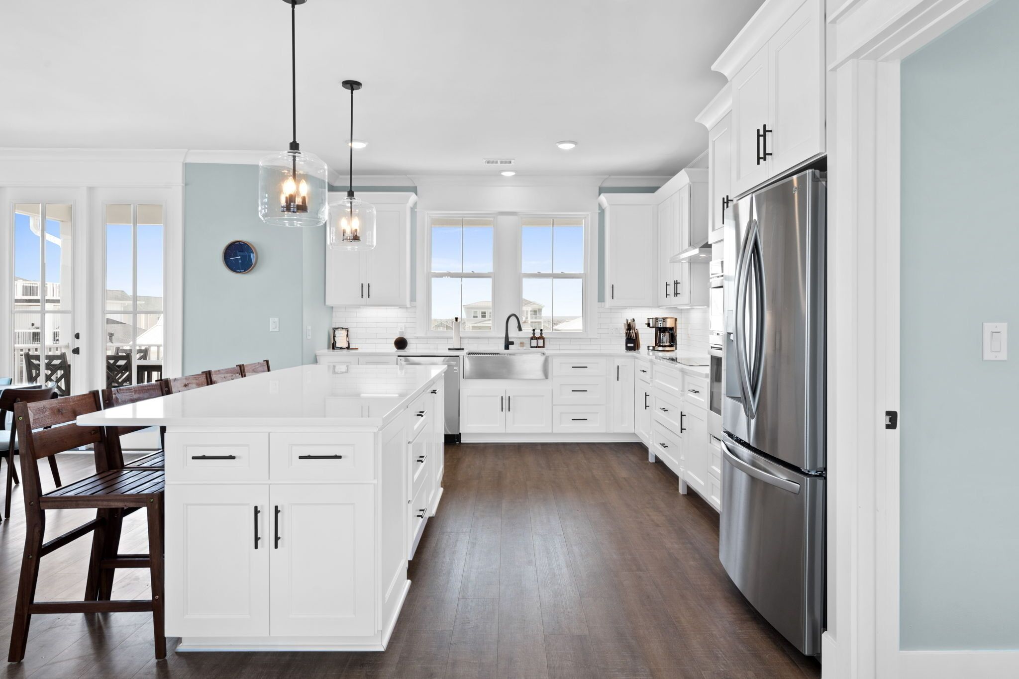 A modern kitchen with white cabinetry, a large stainless steel refrigerator, and a central island with seating.