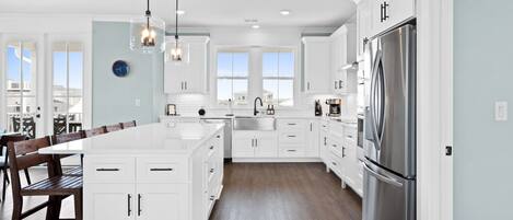 A modern kitchen with white cabinetry, a large stainless steel refrigerator, and a central island with seating.