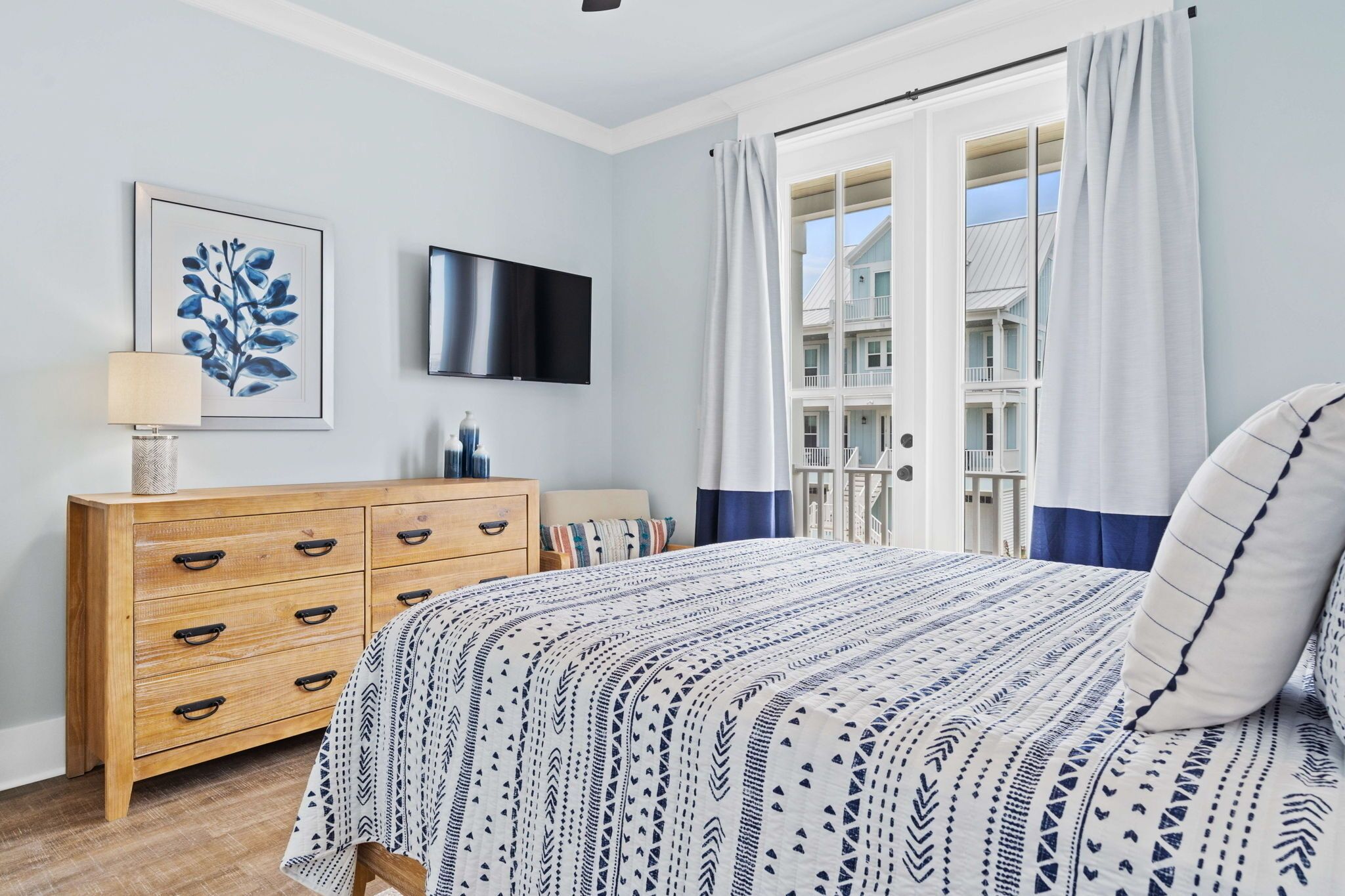 Ein Schlafzimmer mit einem Bett, einer Holzkommode, einem Flachbildfernseher und einem Fenster mit Vorhängen.