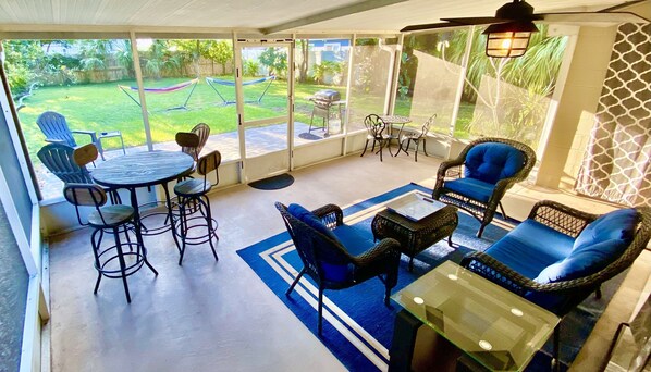 A covered patio with outdoor furniture, a grill, and a view of a backyard.
