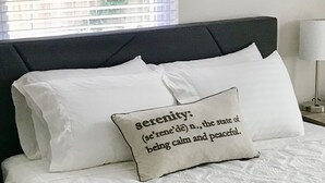 Un lit bien fait, avec une couette blanche et un oreiller orné du mot « sérénité » et de sa définition.