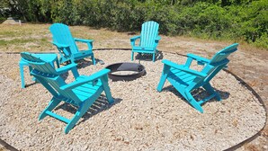 Un espace extérieur circulaire aménagé avec des sièges, comprenant quatre fauteuils Adirondack turquoise et un foyer central.
