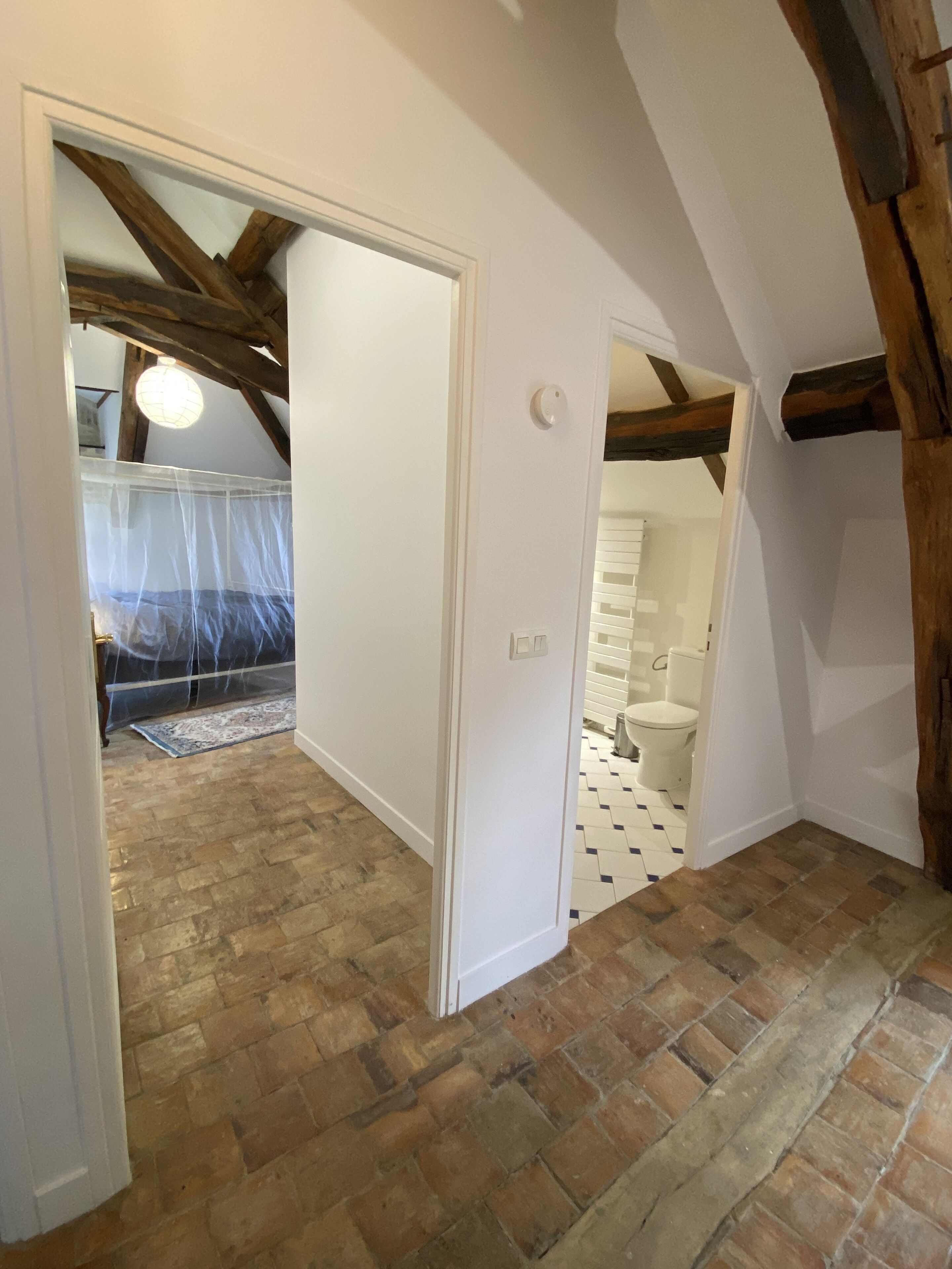 A room with a brick floor, white walls, and exposed wooden beams.