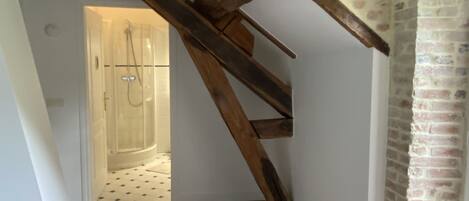 An attic room with exposed wooden beams, a brick floor, and a brick fireplace.