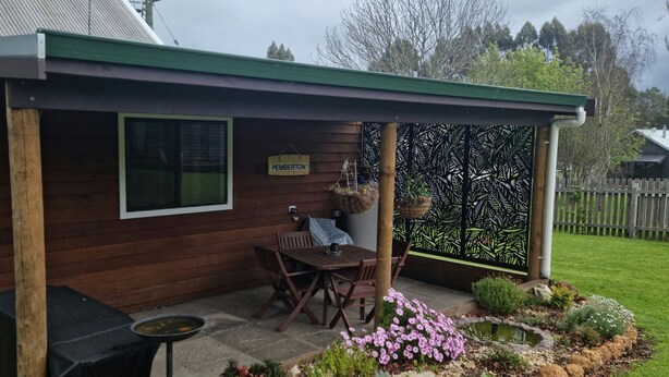 A wooden house with a green roof, a patio with a table and chairs, and a garden with rocks and flowers. - Heritage Timber Cottage - close to shops & amenities (Pemberton)