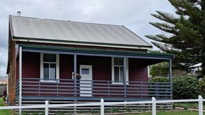 A two-story house with a porch, a white picket fence, and a green roof. - Heritage Timber Cottage - close to shops & amenities (Pemberton)