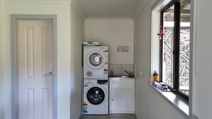 A laundry room with stacked washers and dryers, a small sink, and a window with a view. - Heritage Timber Cottage - close to shops & amenities (Pemberton)