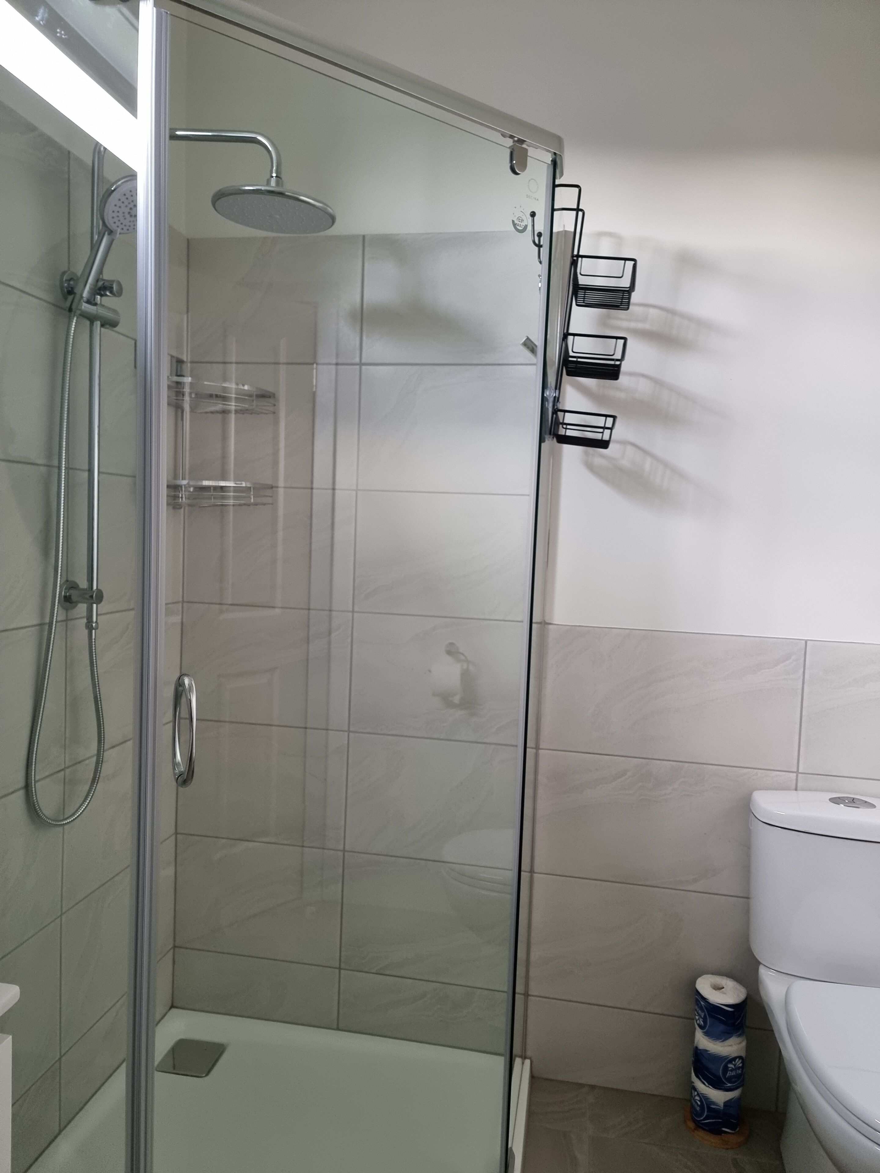 A glass-enclosed shower stall with a handheld showerhead and a wall-mounted faucet.