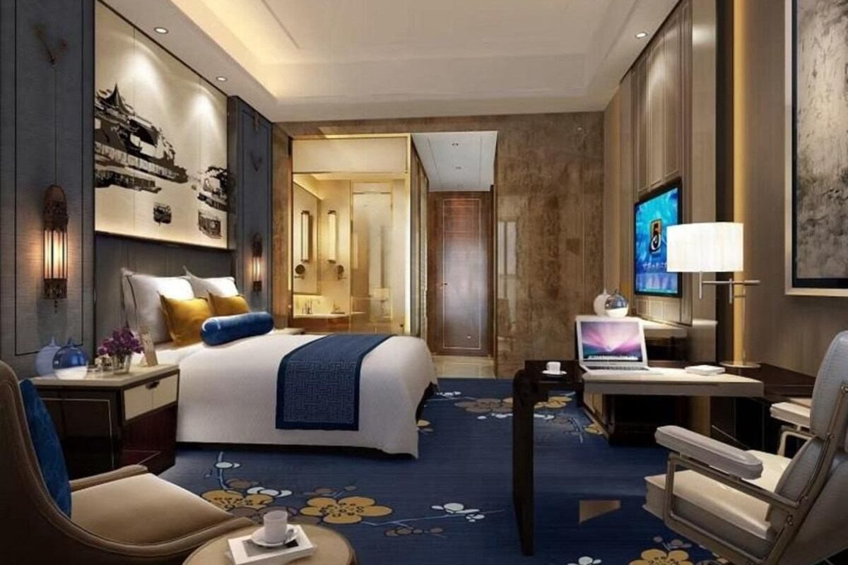 A hotel room with a bed, desk, chair, TV, and artwork on the walls.