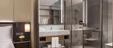 Un baño moderno con ducha de vidrio, lavamanos de mármol y una mesita de noche con un florero.