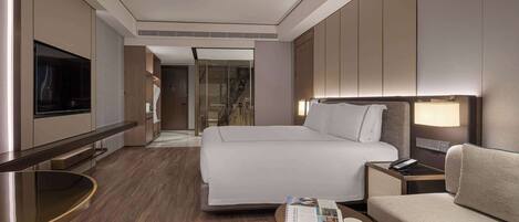 Een moderne hotelkamer met een groot bed, een bank, een klein tafeltje, een televisie en een glazen deur naar een badkamer.