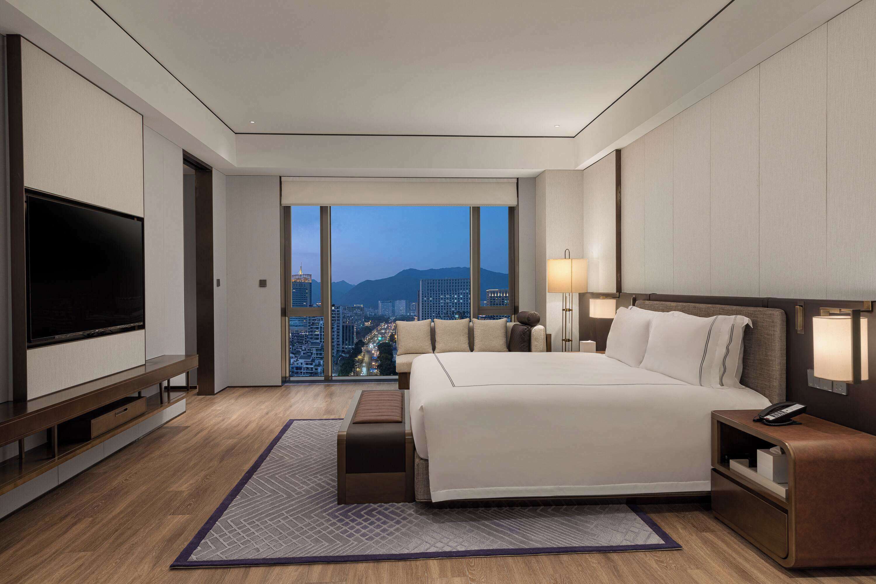 Habitación de hotel moderna con una cama grande, un televisor de pantalla plana, una mesita de noche y vistas a la ciudad.