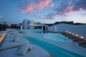A modern pool area with lounge chairs and a hot tub, surrounded by a white building with a view of the sea. - White Stone Mykonos Hotel (Mykonos)