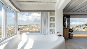 A modern bathroom with a large bathtub, a view of a cityscape, and a wooden ceiling. - White Stone Mykonos Hotel (Mykonos)