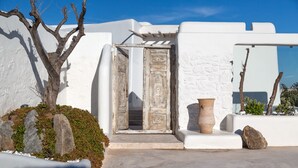 A white building with a wooden door, a stone wall, and a large pot. - White Stone Mykonos Hotel (Mykonos)