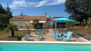 Un jardin à l’arrière d’une maison, avec une piscine, des meubles de jardin et un espace salon abrité.