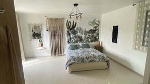 Une chambre spacieuse avec un grand lit, une plante suspendue, un miroir et un luminaire au plafond.
