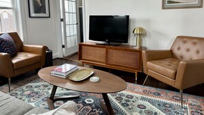 A living room with two leather armchairs, a wooden coffee table with books and a decorative tray, a television on a wooden cabinet, and a patterned rug.
