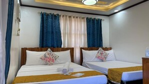Quarto de hotel com duas camas, cabeceira de madeira, luminária no teto e janela com cortinas azuis.