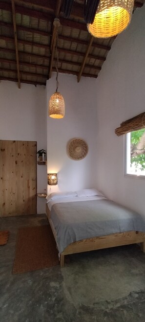 Une chambre avec un lit en bois, une décoration murale en fibres tressées, un luminaire en fibres tressées et une fenêtre donnant sur un paysage verdoyant.