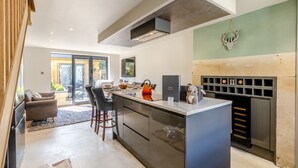 Una cocina moderna con una isla central, horno empotrado y una zona de estar con sofá y sillones.